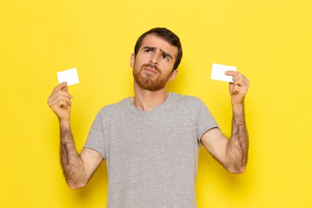 黄色の壁の男式感情カラーモデルに白いカードを保持している灰色のtシャツの正面の若い男性