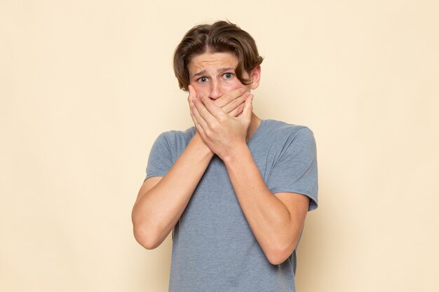 A front view young male in grey t-shirt posing holding his mouth