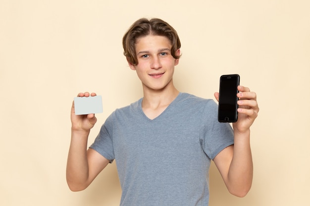 電話とカードを保持しているポーズの灰色のtシャツの正面の若い男性