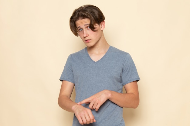 Молодой мужчина в серой футболке, вид спереди, позирует, указывая ему в запястье