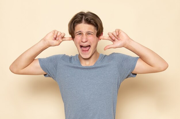 A front view young male in grey t-shirt posing screaming covering his ears