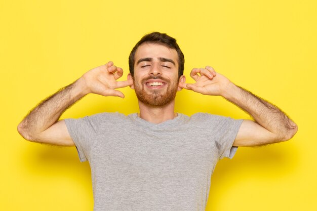 A front view young male in grey t-shirt posing with delighted expression on the yellow wall man color model emotion clothes