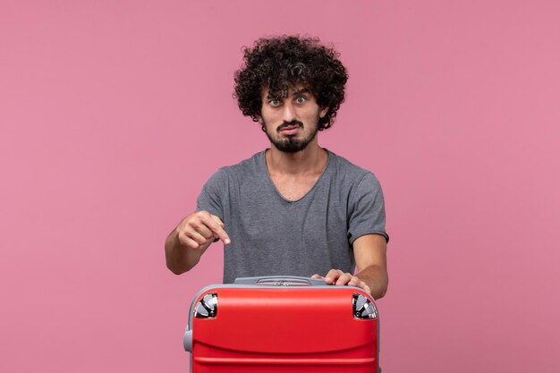 淡いピンクの空間での旅行の準備をしている灰色のTシャツの正面図若い男性