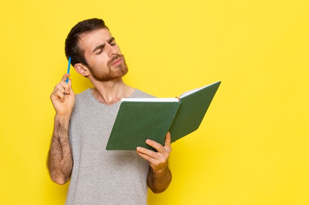 A front view young male in grey t-shirt reading book with thinking expression on the yellow wall man expression emotion color model