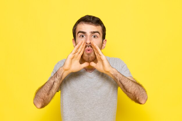 A front view young male in grey t-shirt screaming out on the yellow wall man color model emotion clothes