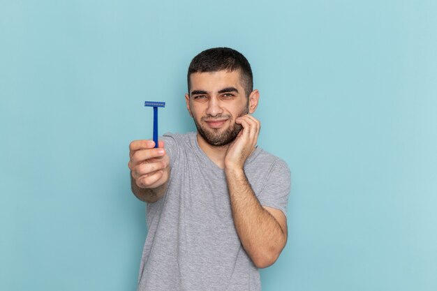 Front view young male in grey t-shirt showing razor on the blue