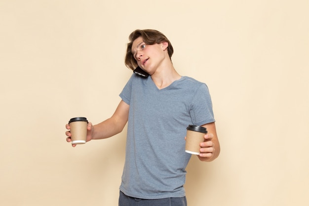 コーヒーカップを保持している電話で話している灰色のtシャツの正面の若い男性