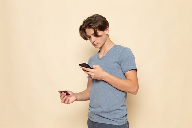 Free photo a front view young male in grey t-shirt using phone and holding card