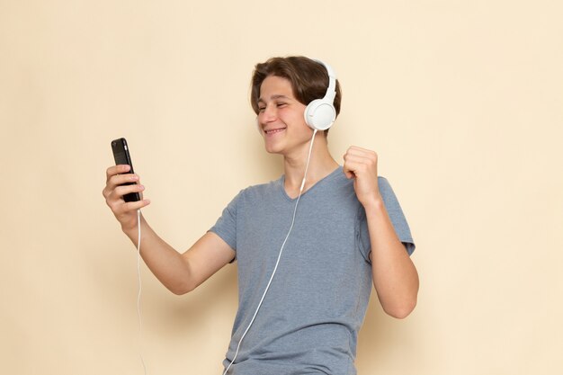 Молодой мужчина в серой футболке с видом спереди разговаривает по телефону и слушает музыку