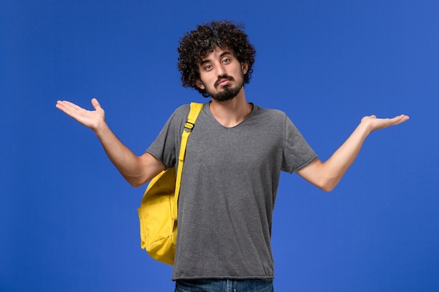 Front view of young male in grey t-shirt wearing yellow backpack on blue wall