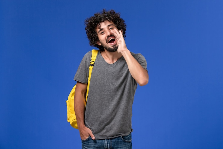 Free Photo front view of young male in grey t-shirt wearing yellow backpack calling out someone on blue wall