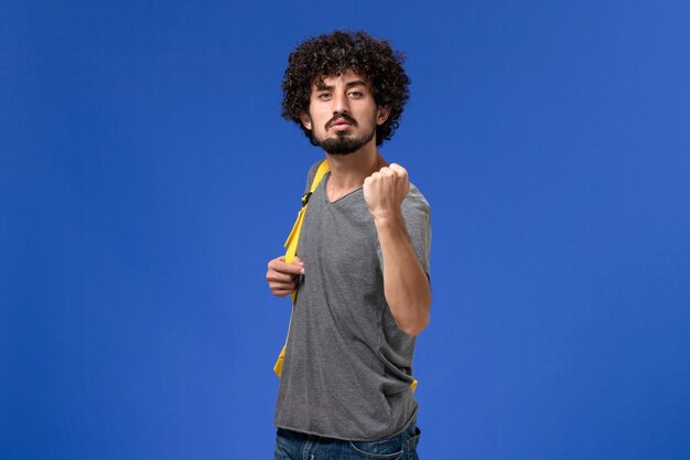 Front view of young male in grey t-shirt wearing yellow backpack just posing on blue wall