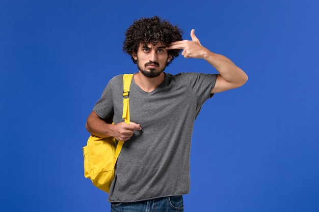 Front view of young male in grey t-shirt wearing yellow backpack just posing on blue wall