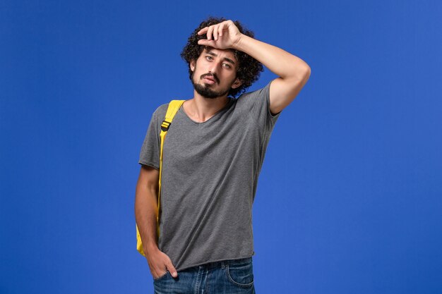 Вид спереди молодого мужчины в серой футболке с желтым рюкзаком, просто позирующего на синей стене