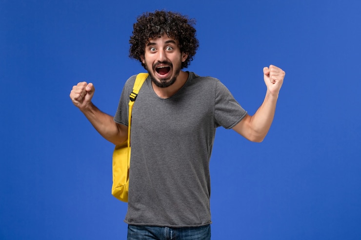 Free Photo front view of young male in grey t-shirt wearing yellow backpack just rejoicing on the blue wall