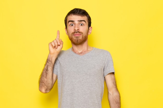 Un giovane maschio di vista frontale in maglietta grigia con un'espressione di idea sul modello di colore di emozione di espressione dell'uomo della parete gialla