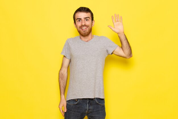 A front view young male in grey t-shirt with raised hand on the yellow wall man expression emotion color model