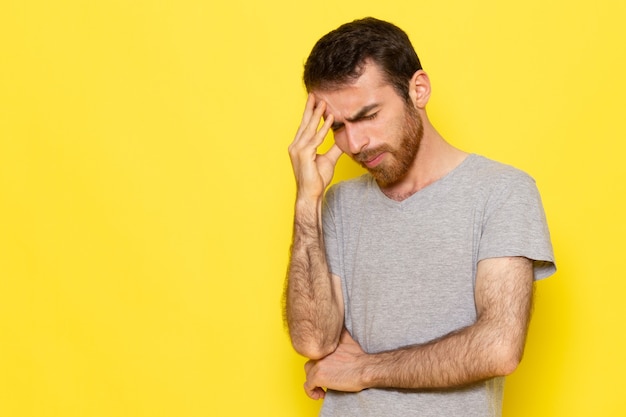 Foto gratuita un giovane maschio di vista frontale in maglietta grigia con l'espressione di pensiero sul colore giallo di emozione di espressione dell'uomo della parete