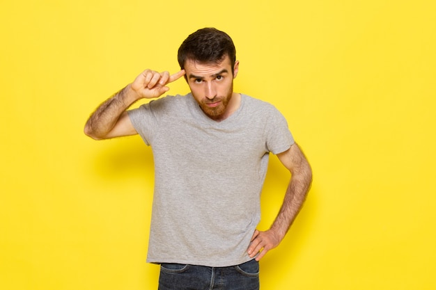 A front view young male in grey t-shirt with thinking expression on the yellow wall man expression emotion color