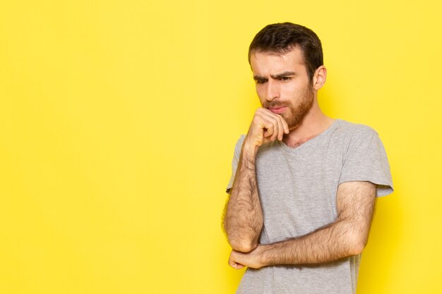 A front view young male in grey t-shirt with thinking expression on the yellow wall man expression emotion color