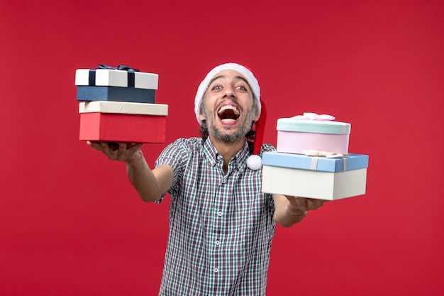 Front view young male happily holding presents on red background