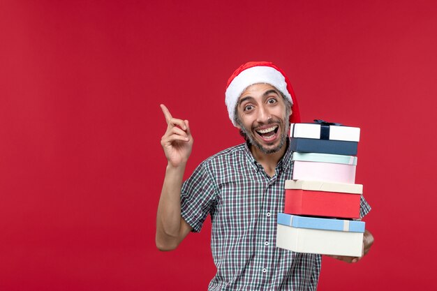 Front view young male happily holding presents on red background