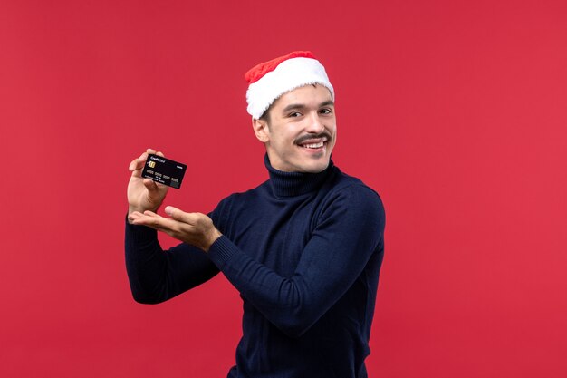 Front view young male holding bank card on red background