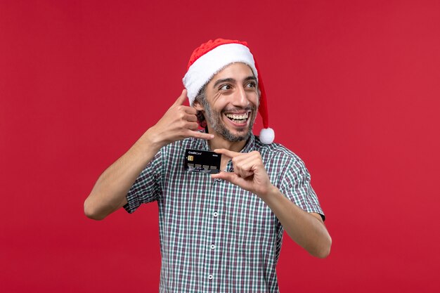 Front view young male holding bank card on red background