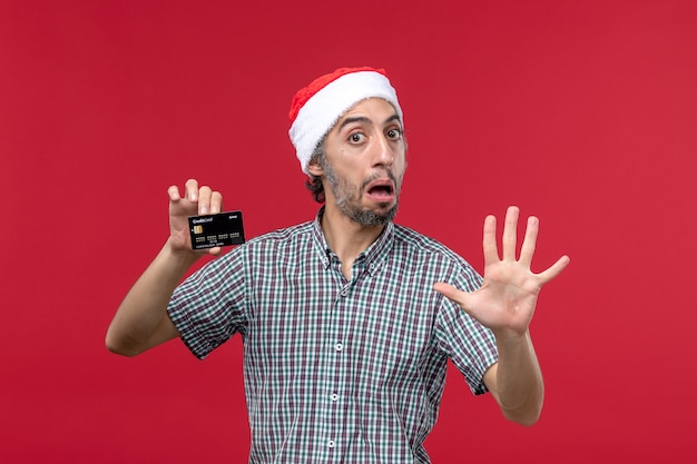 Front view young male holding bank card on red background