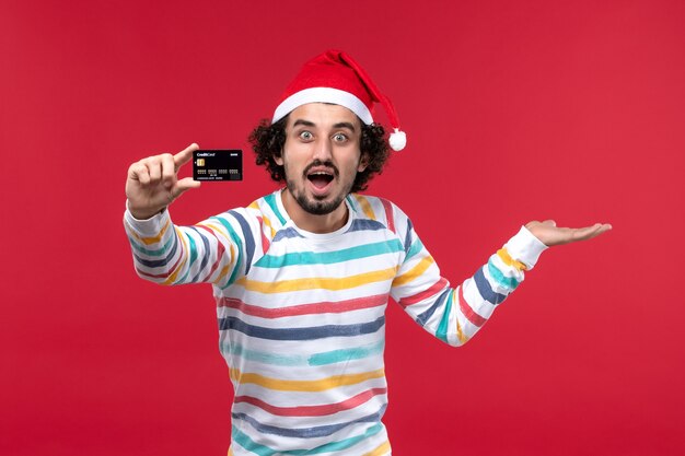 Front view young male holding bank card on red wall emotion red male holidays