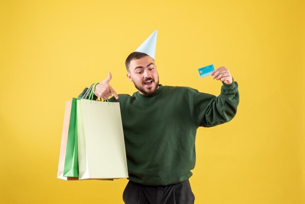 黄色の背景に銀行カードとショッピングパッケージを保持している若い男性の正面図