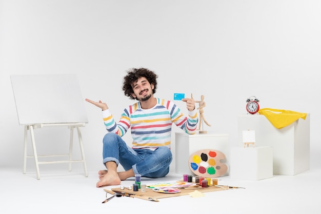 Front view of young male holding bank card on white wall