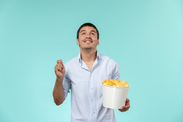 Вид спереди молодого мужчины, держащего корзину с картофельными чипсами на синем столе