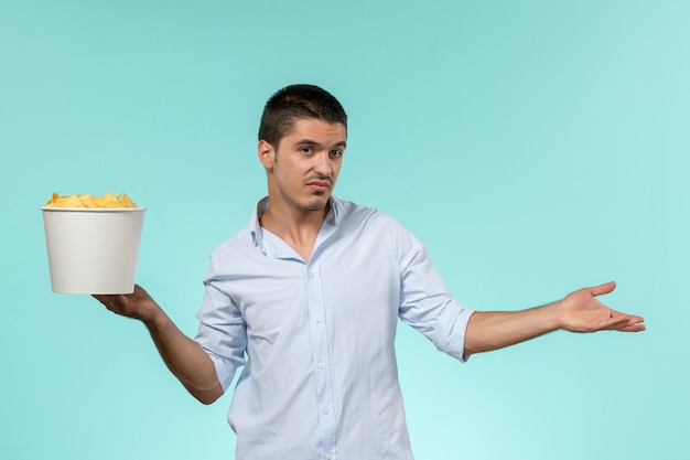 Вид спереди молодого мужчины, держащего корзину с картофельными чипсами на синей поверхности