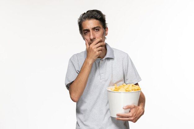 Вид спереди молодой мужчина, держащий корзину с картофельными чипсами на белом полу, мужской удаленный кинотеатр, одинокий
