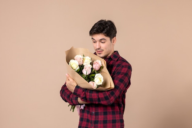 Вид спереди молодой мужчина держит красивые цветы на коричневой стене