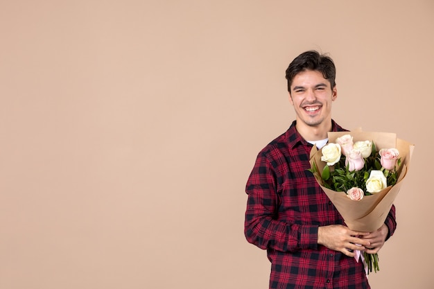 茶色の壁に美しい花を保持している正面図若い男性
