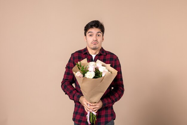 Front view young male holding beautiful flowers on brown wall