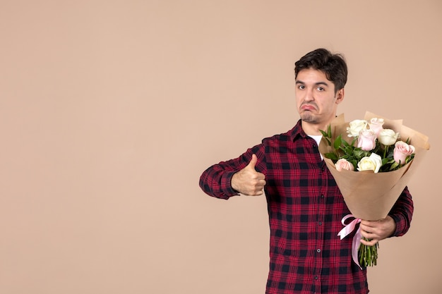 Free photo front view young male holding beautiful flowers on brown wall