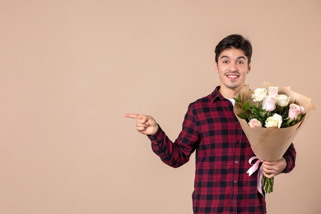 Front view young male holding beautiful flowers on brown wall