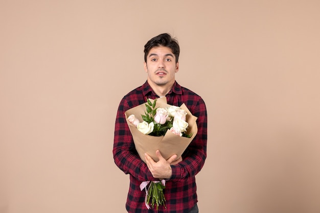 茶色の壁に美しい花を保持している正面図若い男性