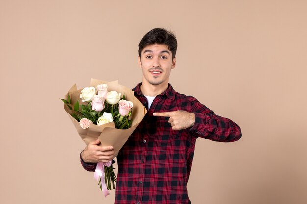 Front view young male holding beautiful flowers on brown wall