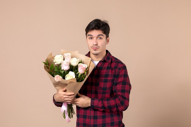 Front view young male holding beautiful flowers on brown wall