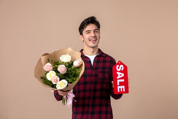 Front view young male holding beautiful flowers and sale nameplate on brown wall