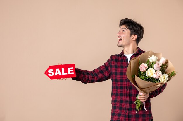 Front view young male holding beautiful flowers and sale nameplate on brown wall