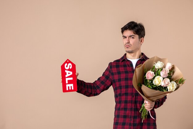 Front view young male holding beautiful flowers and sale nameplate on brown wall