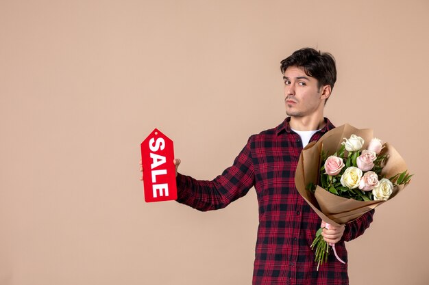 Front view young male holding beautiful flowers and sale nameplate on brown wall