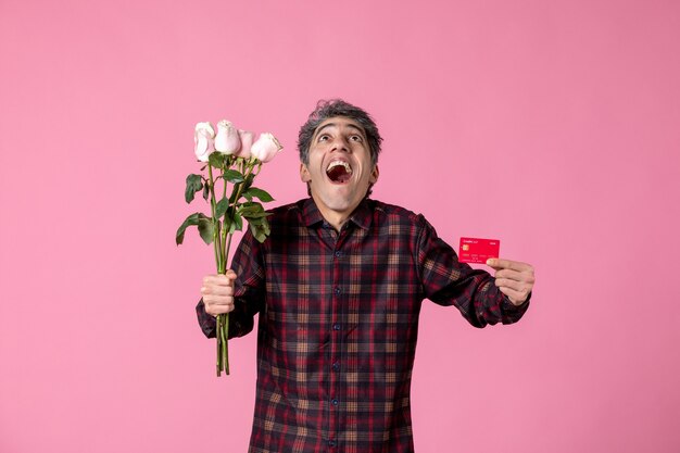 Front view young male holding beautiful pink roses and bank card on pink wall