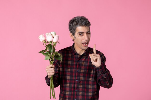 Front view young male holding beautiful pink roses on pink wall