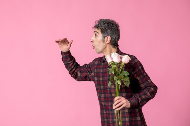 ピンクの壁に美しいピンクのバラを保持している正面図若い男性